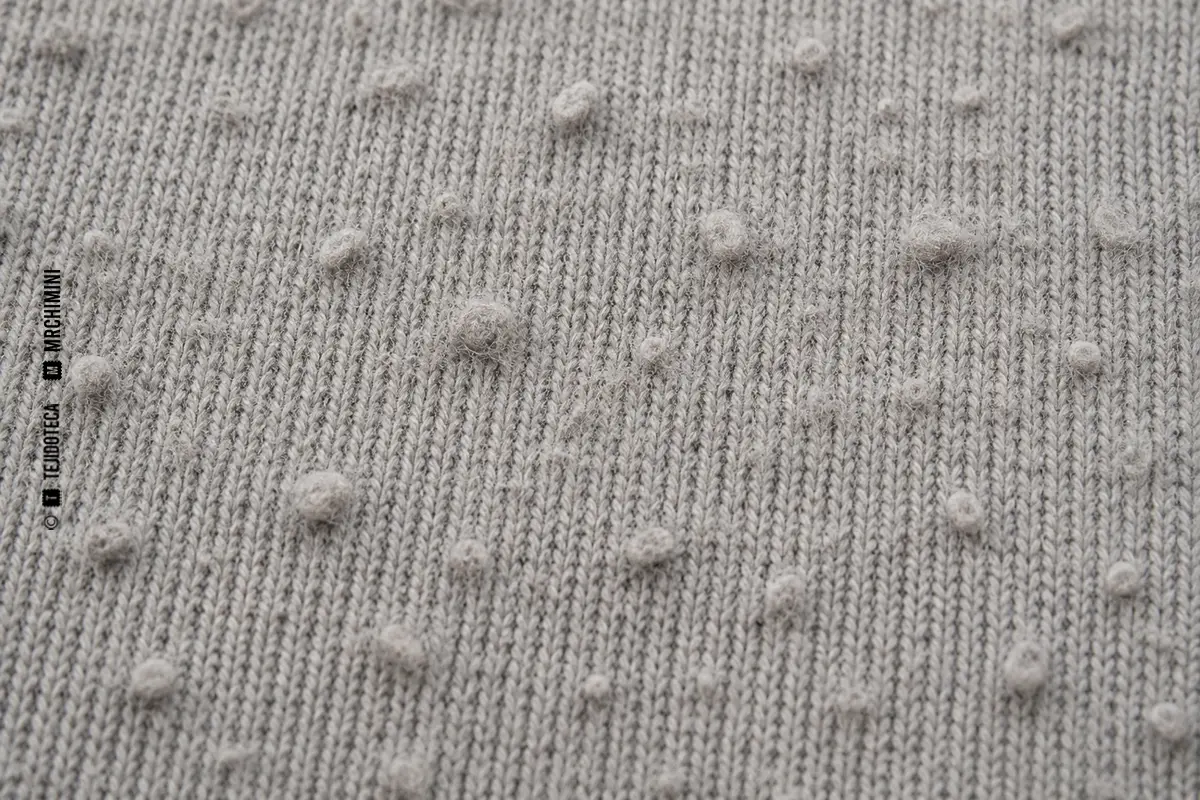 Pilling visible en la superficie de un tejido de punto gris, con pequeñas bolitas de fibras.