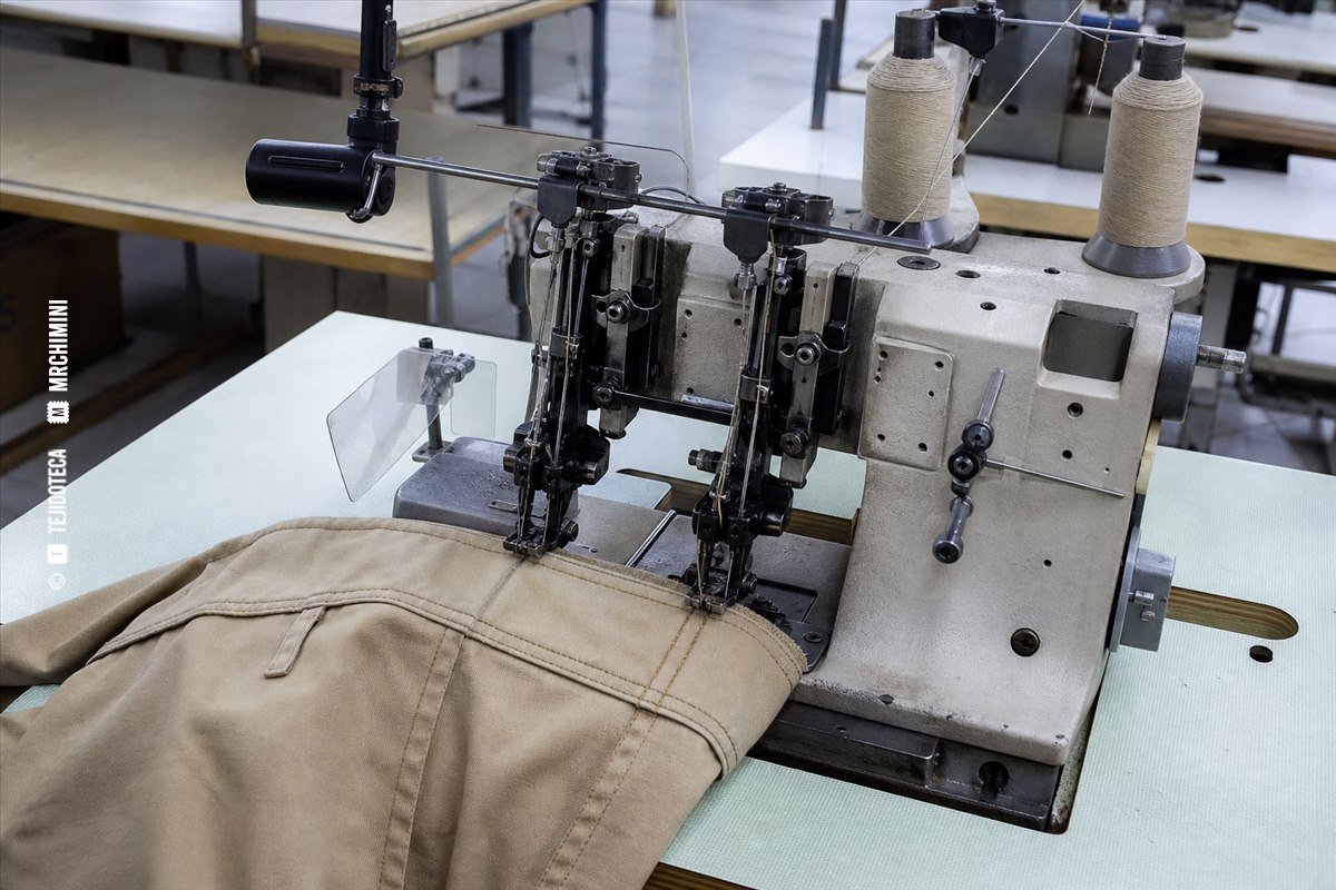 Máquina industrial de cadeneta realizando costuras paralelas en un pantalón