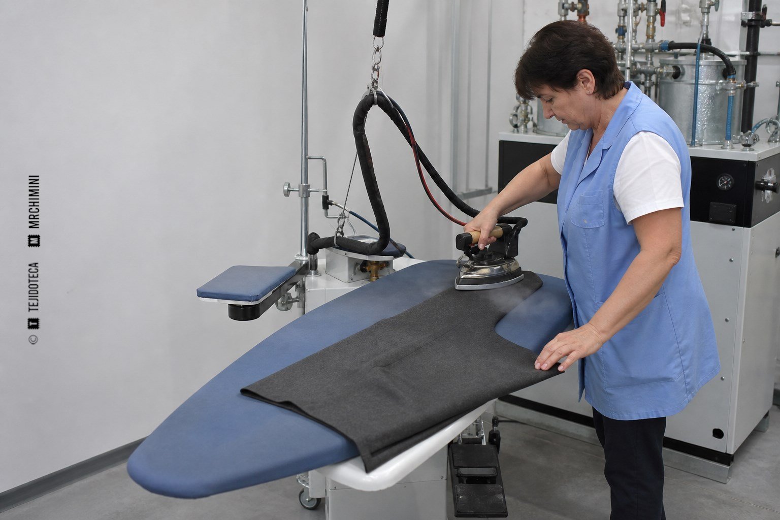 Plancha industrial de vapor trabajando sobre una mesa aspirante en una fábrica de confección