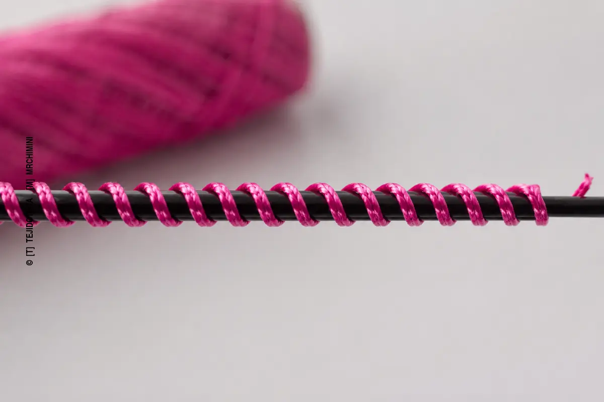 HILO RECUBIERTO – detalle macro Detalle macro de un hilo recubierto con núcleo negro y filamento fucsia enrollado helicoidalmente.