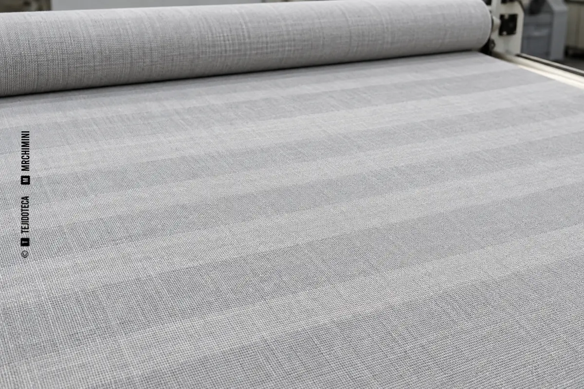 Tejido gris inspeccionado sobre mesa con bandas periódicas visibles en todo su ancho
