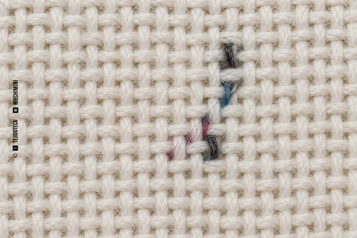 Macro de tejido blanco con pequeñas fibras oscuras y coloreadas incorporadas en la estructura