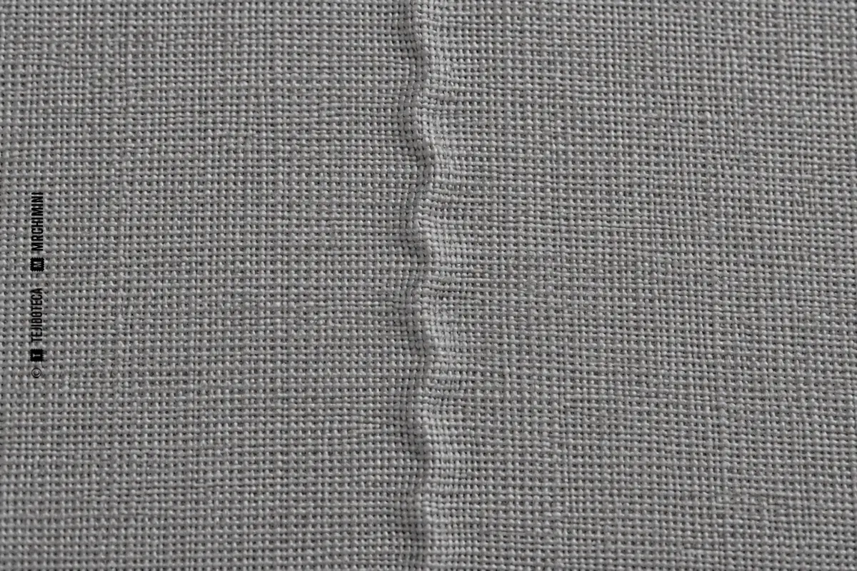 Macro de tejido gris con un cabo de urdimbre presente, ondulado y ligeramente elevado por baja tensión