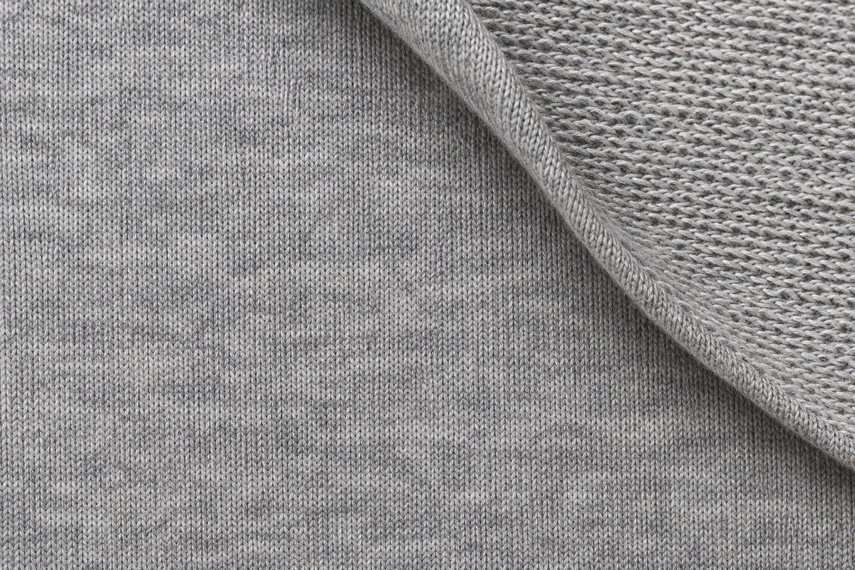 Detalle ampliado de French terry gris con cara lisa de punto y una esquina vuelta que muestra los bucles del reverso sin perchar