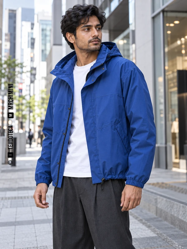 Hombre con parka azul cobalto y pantalón gris; una tanca regula el cordón del bajo.