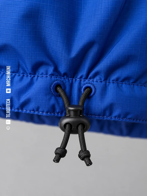 Detalle del túnel del bajo de una parka azul, con salidas de cordón, tanca negra y extremos rematados.