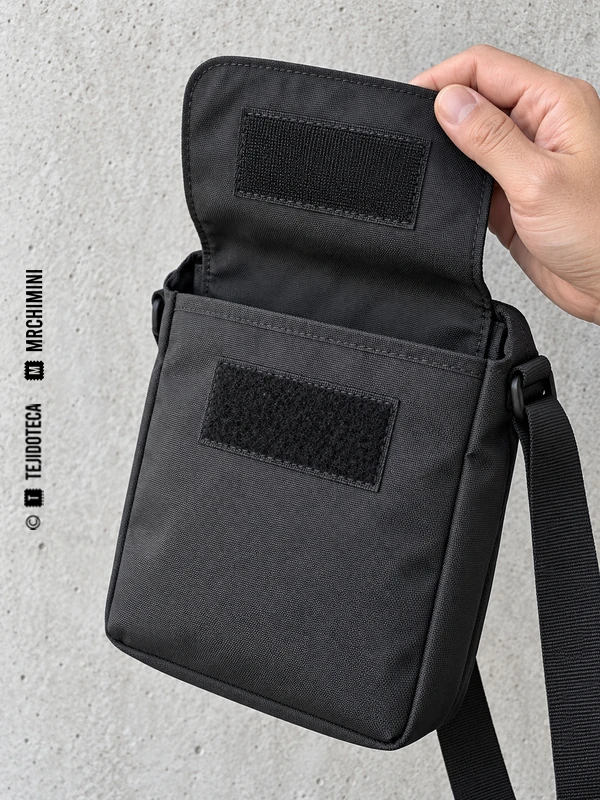 Bolso negro con la solapa abierta y dos piezas de cierre de gancho y bucle cosidas.