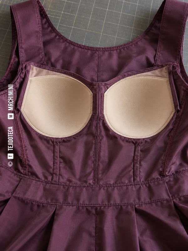 Revés de un cuerpo de vestido ciruela con un par de copas claras fijadas al forro.