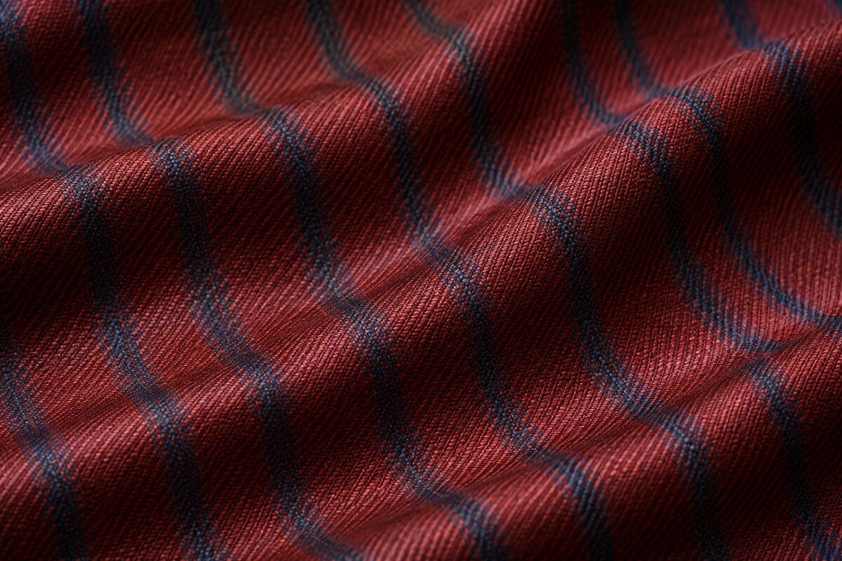 Detalle macro de calamaco de lana en rojo granate y azul, con superficie lustrosa y rayas tejidas
