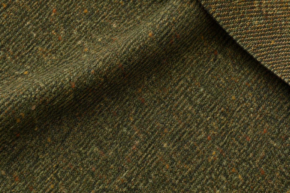 Macro de tweed verde con diagonal fina, notas ocres y rojizas y una esquina vuelta